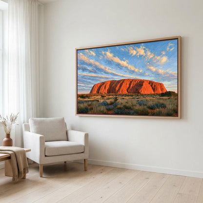 a large framed painting of Uluru, a famous red rock formation in Australia, hanging on a white wall in a living room.