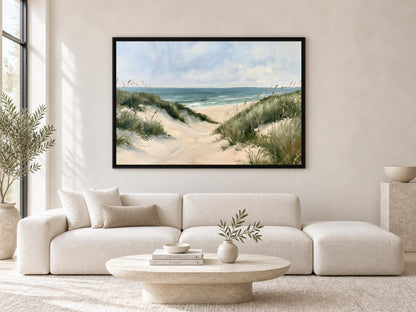 a living room with a large painting of a beach scene hanging on the wall above a white sofa. The painting depicts a sandy beach with dunes and the ocean in the background. The room has a minimalist and modern design, with a round coffee table in the center and a potted plant on the left side.