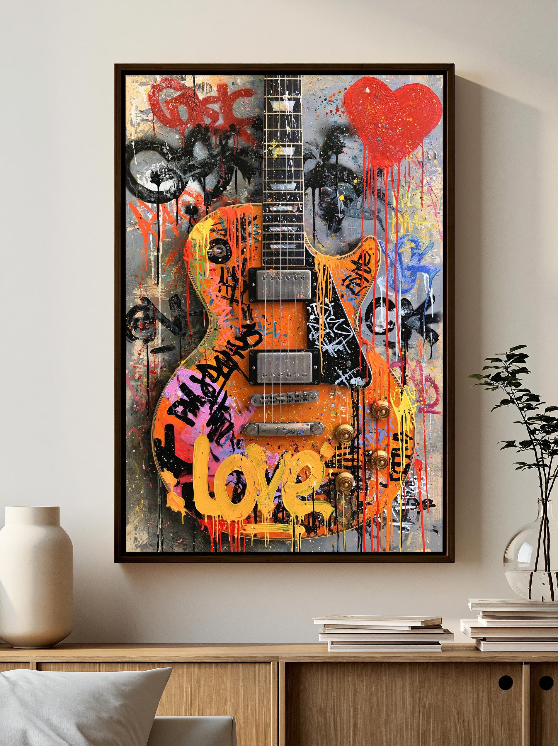 a vibrant and colorful graffiti-style artwork of a guitar, with the word "love" prominently displayed in the center. The artwork is framed and hung on a wall, with a bookshelf and a vase visible in the background.