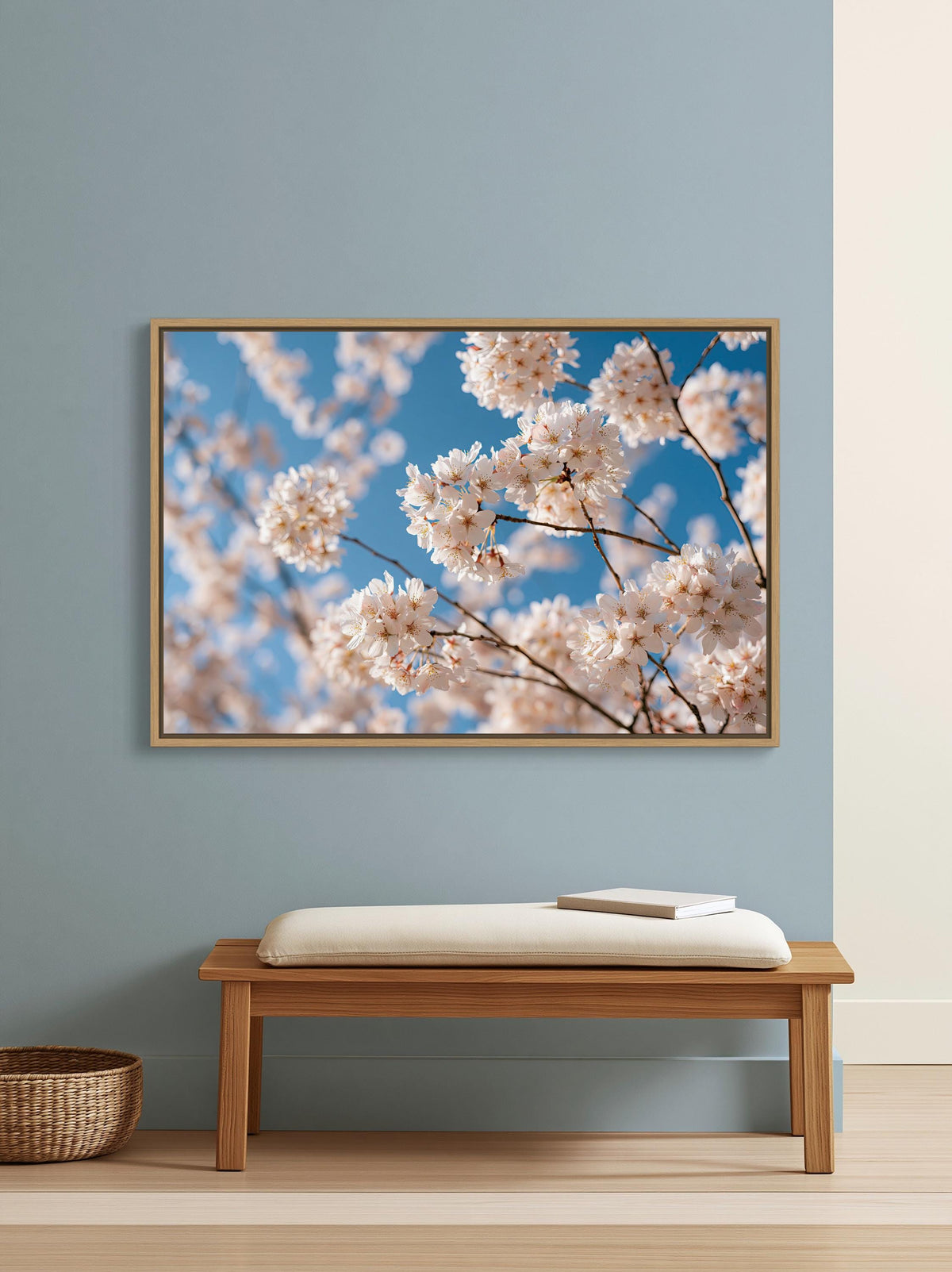 Cherry blossom branches canvas wall art, wooden bench with a white cushion, positioned in front of a framed picture of