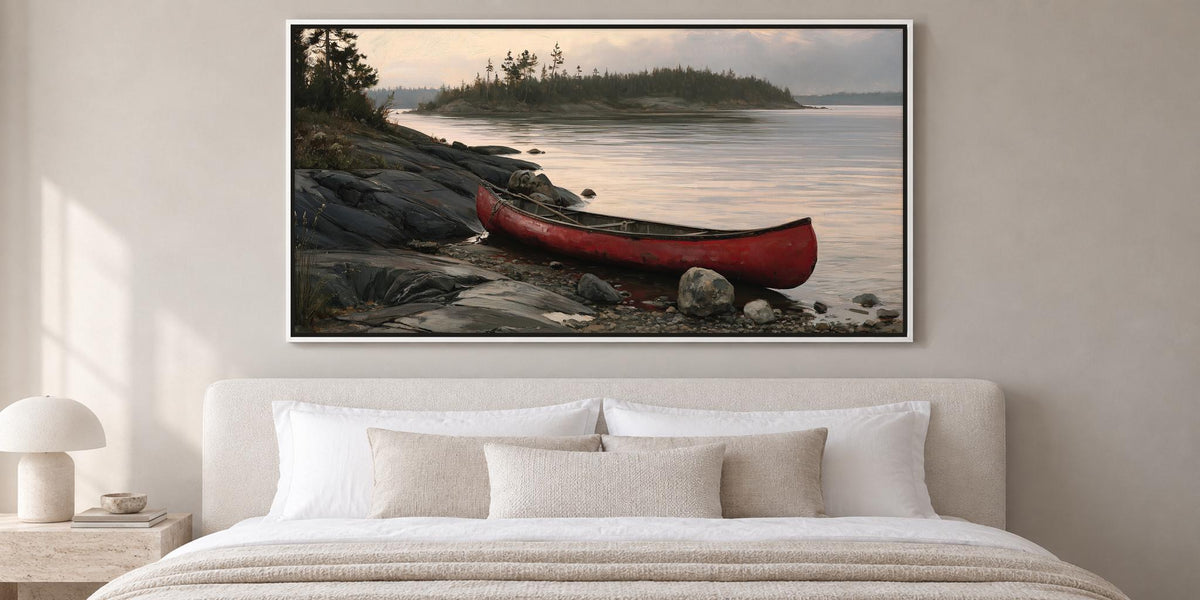 A large framed painting depicting a red canoe resting on a rocky shore, with a calm lake and trees in the background.