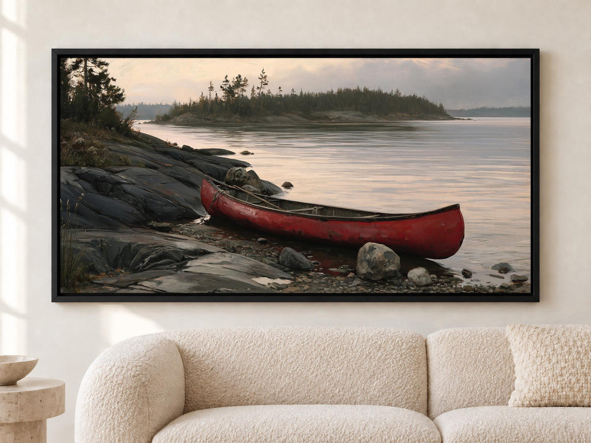 A large framed painting depicting a red canoe resting on a rocky shore, with a calm lake and trees in the background.