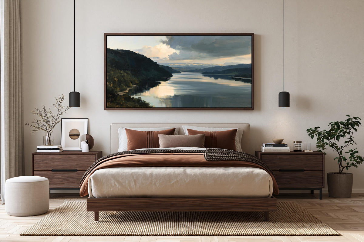 a serene bedroom with a large bed, wooden furniture, and a framed landscape painting hanging above it. The room has a neutral color scheme with beige walls, a brown wooden floor, and a white ottoman. The painting features a tranquil scene of a lake surrounded by mountains, creating a peaceful and relaxing atmosphere.