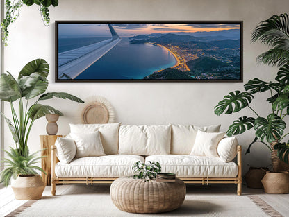 a large, framed picture of an airplane wing with a stunning aerial view of a coastal city at sunset.