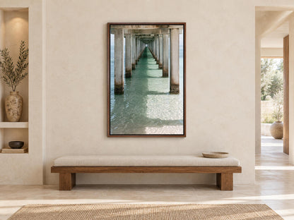 a serene indoor setting with a wooden bench, a large framed picture of a pier or walkway, and a vase on a shelf. The overall atmosphere appears to be calm and peaceful, with the wooden bench and the framed picture providing a sense of comfort and relaxation.