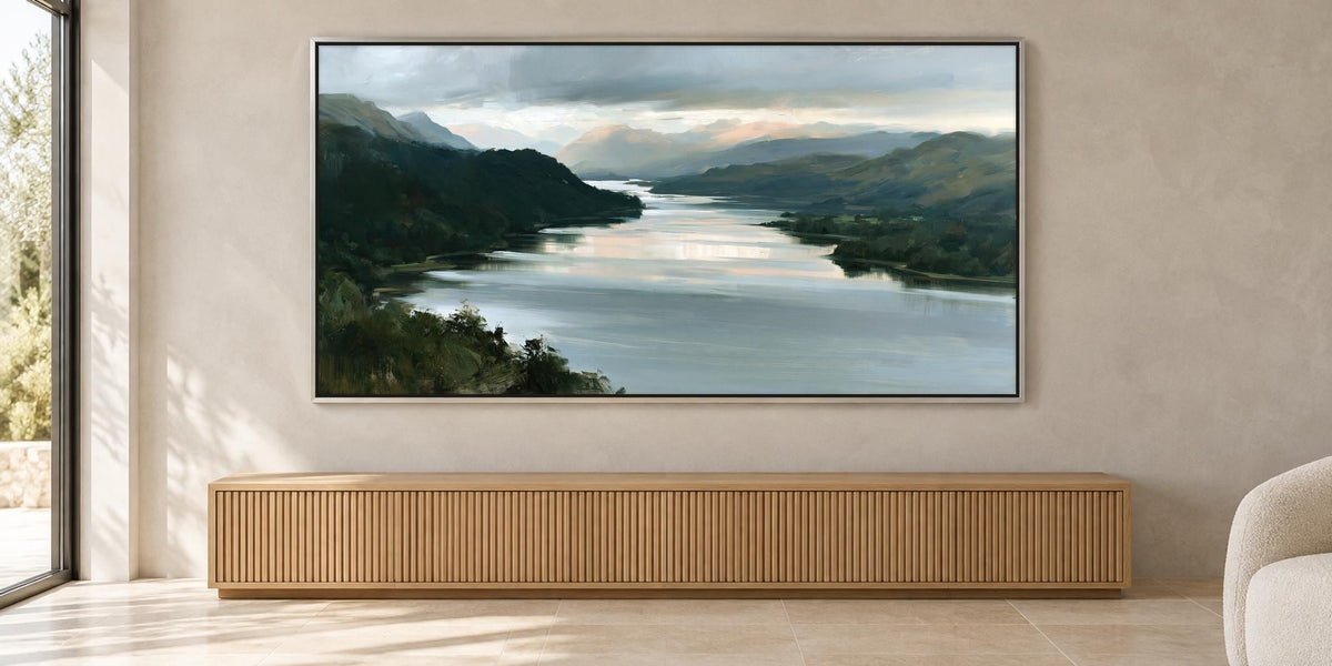a large painting of a serene landscape with a river and mountains in the background, hanging on a wall above a wooden cabinet or console.