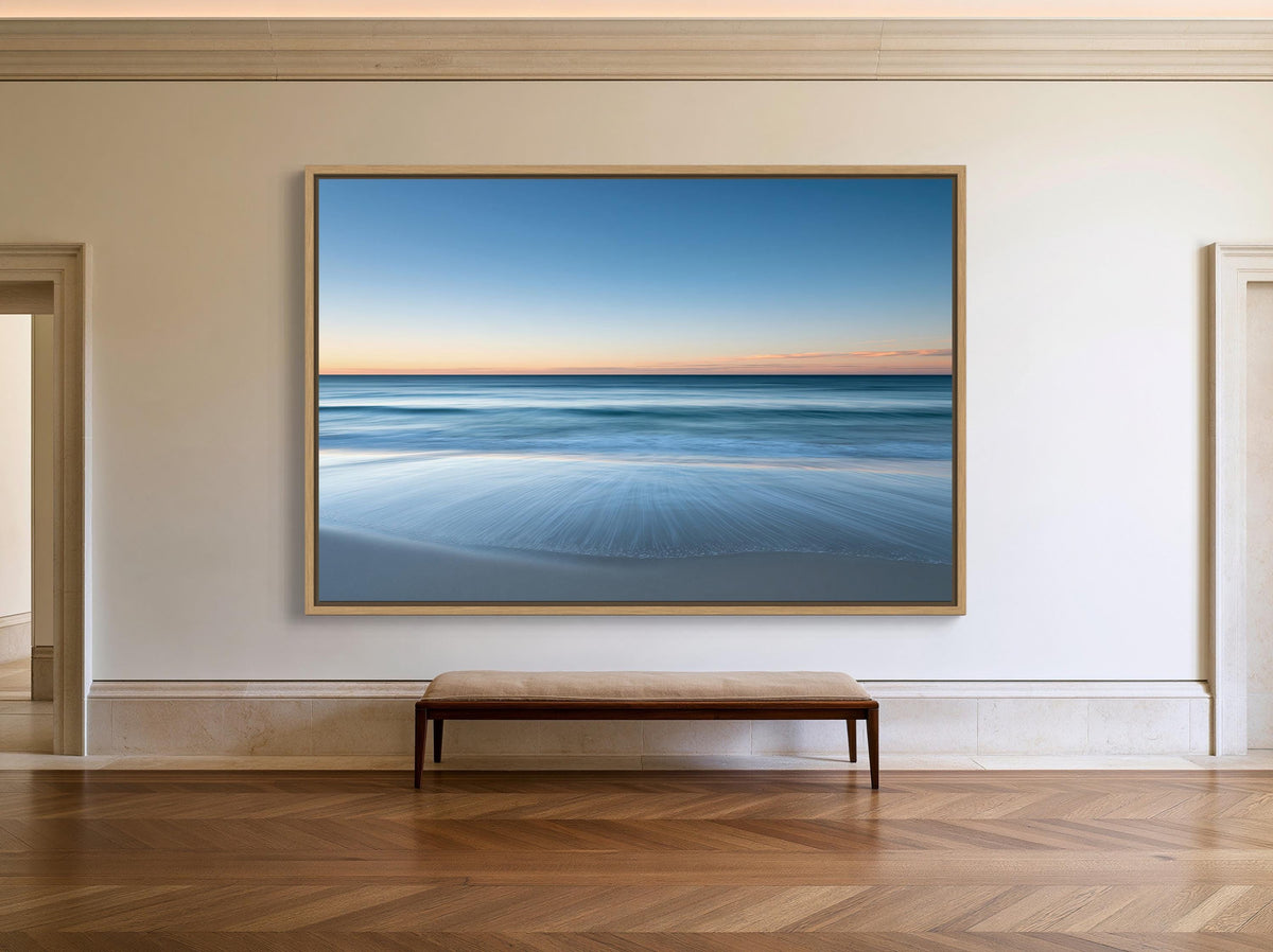 Ocean horizon at dusk canvas wall art, large, square painting of a serene beach scene hanging on a white wall. In front of