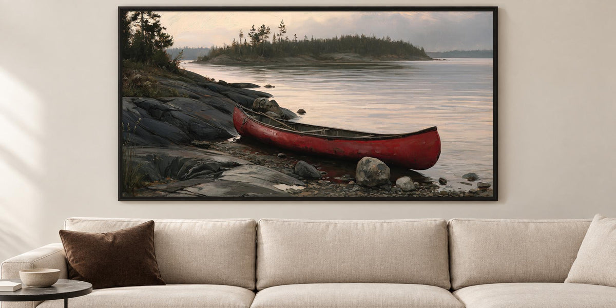 A large framed painting depicting a red canoe resting on a rocky shore, with a calm lake and trees in the background.