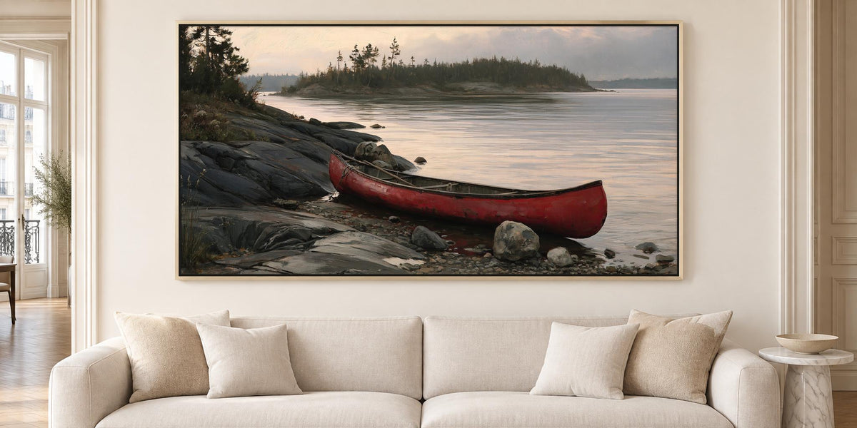 A large framed painting depicting a red canoe resting on a rocky shore, with a calm lake and trees in the background.