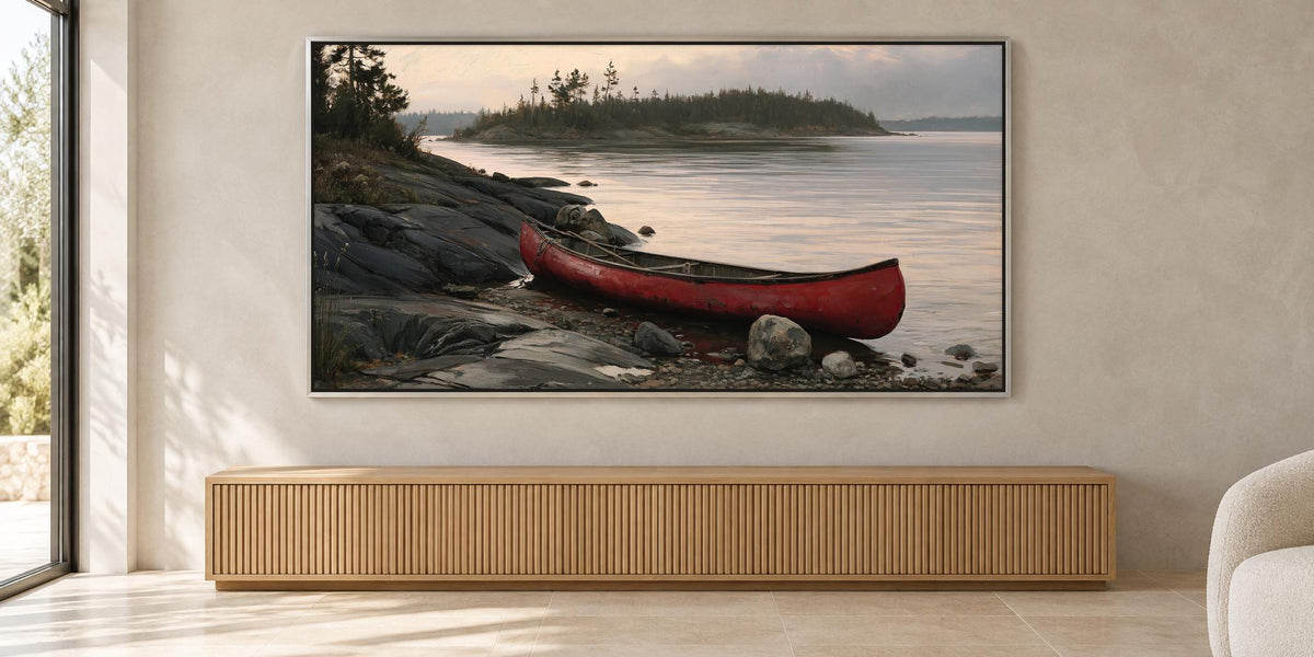 A large framed painting depicting a red canoe resting on a rocky shore, with a calm lake and trees in the background.