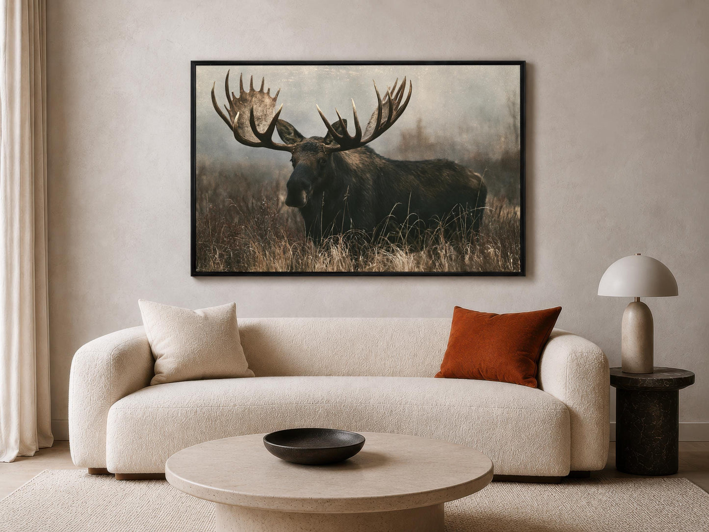a large framed photograph of a moose with large antlers, mounted on a wall above a beige sofa in a living room setting.